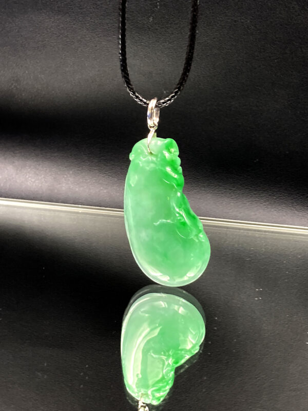 A stunning close-up of the Natural Jadeite Melon Pendant, showcasing its vibrant green hue and intricate vine-and-leaf carvings. The 18K white gold clasp adds a luxurious contrast, resting elegantly on a black woven rope (chain sold separately).