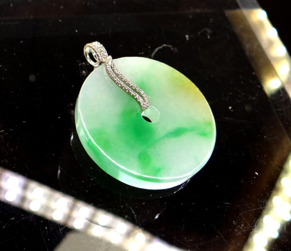 A stunning Natural Jade Peace Pendant featuring a smooth, translucent jade center with a warm green hue, elegantly framed by an 18K white gold clasp adorned with pavé-set diamonds.