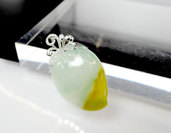 A stunning close-up of the Natural Ice-type Yellow Jadeite Peach Pendant, showcasing its translucent ice-like texture, warm yellow hues, and intricate 18K white gold and diamond clasp.