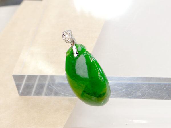 A stunning close-up of a full-green jadeite melon-shaped pendant with intricate carving, paired with a polished 18K white gold clasp, resting on a velvet background.