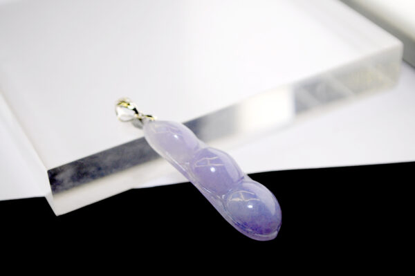 A stunning close-up of the translucent violet jade bean pendant, intricately carved and paired with a sparkling 18K white gold diamond clasp, resting on a velvet background.