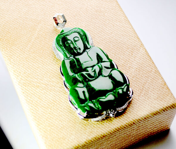 A stunning close-up of the Natural Full-Green Jadeite Avalokitesvara Pendant, showcasing its deep green hue, intricate carvings, and sparkling diamond accents set in 18K white gold. The pendant rests elegantly on a velvet background, highlighting its luxurious craftsmanship.