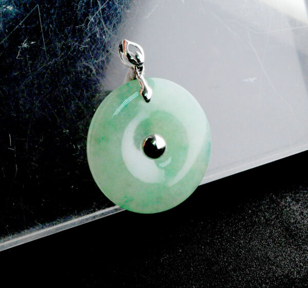 A stunning close-up of the Natural Ice Green Jade Peace Button Pendant, showcasing its ice-green hue and 18K white gold inlay. The pendant's smooth edges and intricate design highlight its craftsmanship and elegance.
