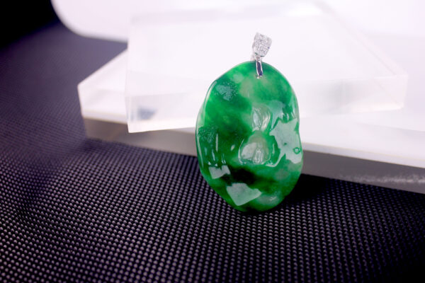 A stunning "Spicy Green" old pit emerald pendant featuring intricate "Enlightenment" carving, set in 18K white gold with sparkling diamond accents. The deep green gemstone contrasts elegantly with the gleaming metal.