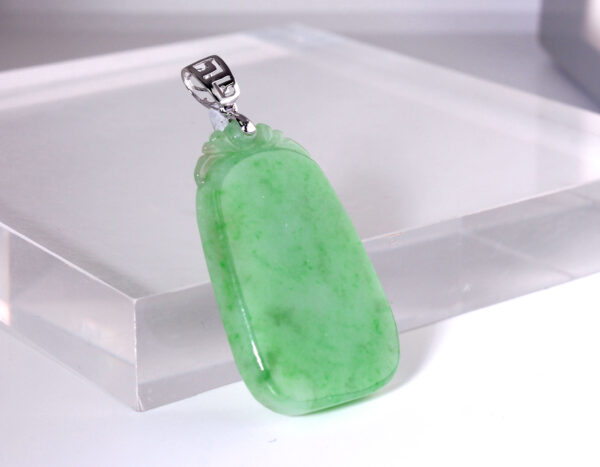 A close-up of the Natural Jadeite Ice Bean Plain Pendant, showcasing its fresh green hue, smooth polished surface, and intricate silver clasp against a neutral background.