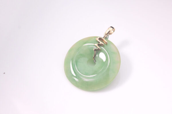 A stunning close-up of the Natural Emerald Peace Button Pendant, showcasing its vibrant yellow-and-green gradient emerald set in polished 18K yellow gold. The pendant's smooth, rounded design and delicate wavy embellishments highlight its elegance and craftsmanship.