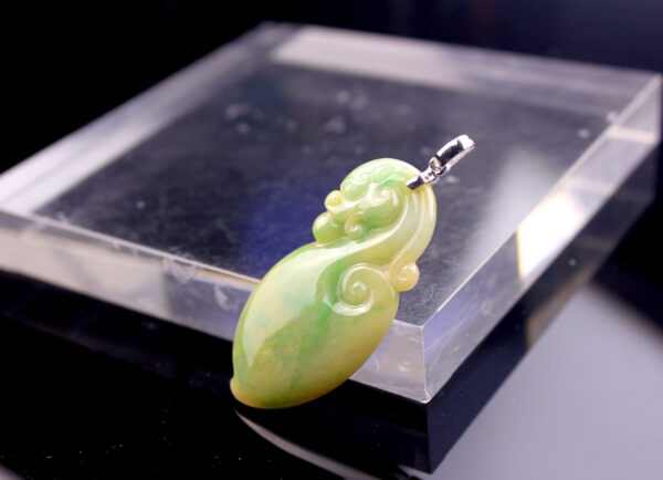 A stunning close-up of the Natural Yellow-Green Jadeite Dragon Pendant, showcasing its smooth gradient of warm yellow and vibrant green hues, intricately carved antique dragon design, and lustrous 18K white gold clasp.
