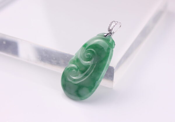 A stunning close-up of the Natural Flower Jade Ruyi Pendant, showcasing its vibrant green hue and intricate 18K white gold diamond clasp. The jade’s natural patterns and the diamonds’ sparkle are highlighted under soft lighting.