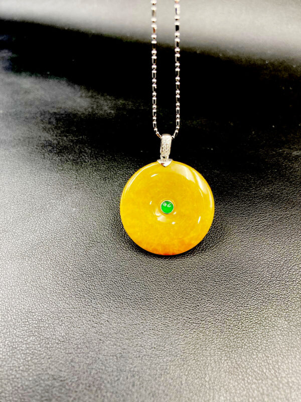 A stunning close-up of the Natural Emerald Ice Yellow Peace Pendant, showcasing its smooth, rounded silhouette and translucent ice-yellow hue with delicate green accents. The pendant rests elegantly on a neutral background, highlighting its traditional craftsmanship and modern appeal.