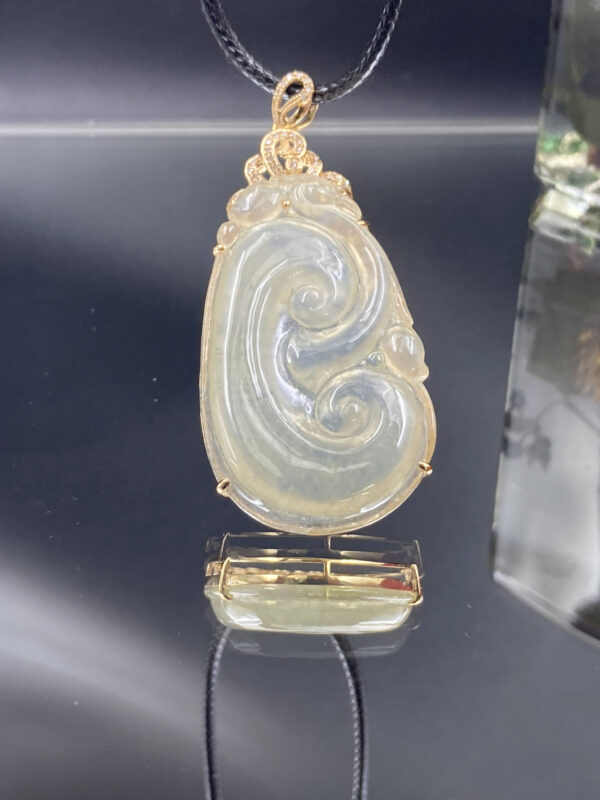 A stunning close-up of the Natural Ice-white Jade Ruyi Pendant, showcasing its delicate 18K yellow gold inlay and intricate Ruyi carving. The jade's translucent, ice-like sheen contrasts beautifully with the warm gold tones.