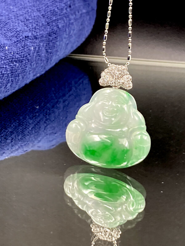 A stunning close-up of the Natural Jadeite Ice-white Buddha Pendant, showcasing its delicate floating green patterns on a translucent base. The 18K white gold diamond clasp sparkles elegantly, highlighting the intricate craftsmanship.