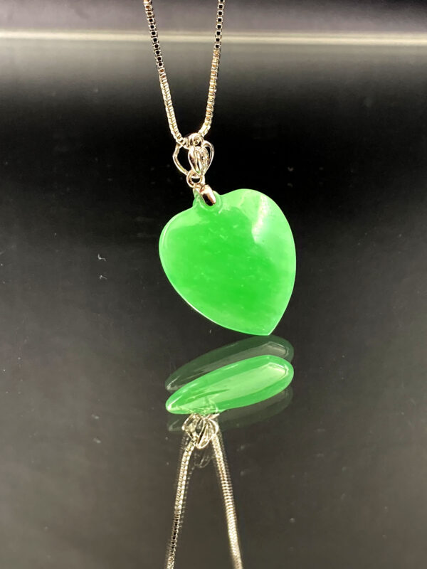 A stunning Natural Emerald Heart Pendant featuring a full-green, ice-type emerald carved into a smooth apricot heart shape, set in luxurious 18K white gold with delicate diamond accents. The pendant glistens under light, showcasing its rich color and exquisite craftsmanship.