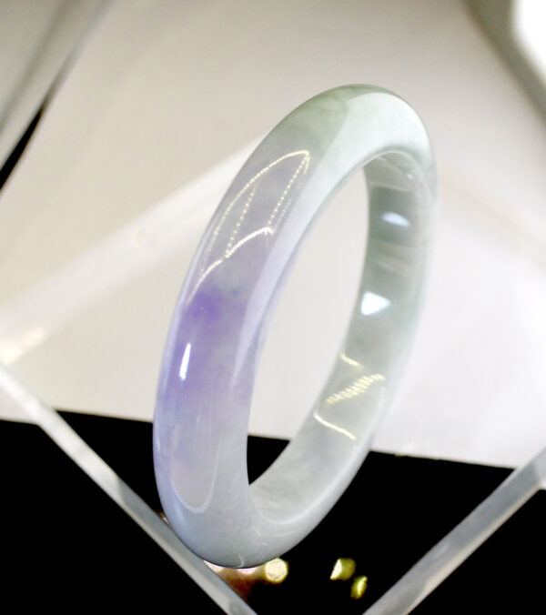 A stunning Natural Violet Jadeite Bracelet with a smooth, polished surface, showcasing a harmonious blend of violet and pale green hues. The round-shaped design fits comfortably on the wrist, radiating a warm, glassy luster.