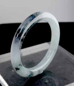 A stunning Natural Ice-type Black Chicken Jade Bracelet resting on a silk cloth, showcasing its ice-clear base and elegant ink-like veins. The smooth, polished surface reflects light beautifully, highlighting its natural artistry.