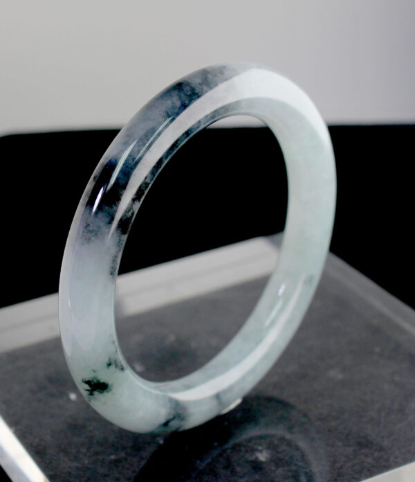 A stunning Natural Ice-type Black Chicken Jade Bracelet resting on a silk cloth, showcasing its ice-clear base and elegant ink-like veins. The smooth, polished surface reflects light beautifully, highlighting its natural artistry.