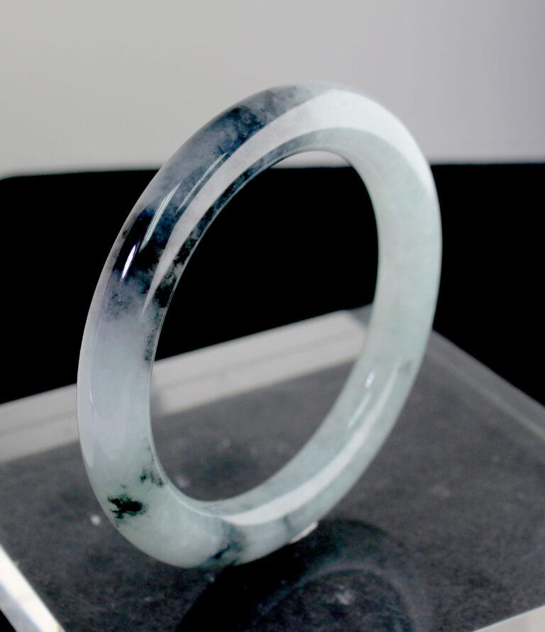 A stunning Natural Ice-type Black Chicken Jade Bracelet resting on a silk cloth, showcasing its ice-clear base and elegant ink-like veins. The smooth, polished surface reflects light beautifully, highlighting its natural artistry.