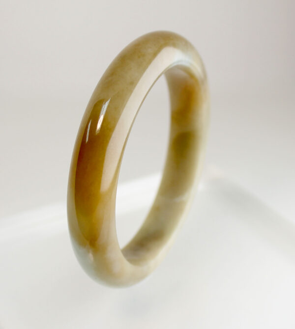 A radiant Natural Yellow Jadeite Bracelet with a smooth, polished surface, showcasing a gradient of warm amber tones. The elegant round-bar design rests gracefully on a wrist, reflecting light with a glassy luster.