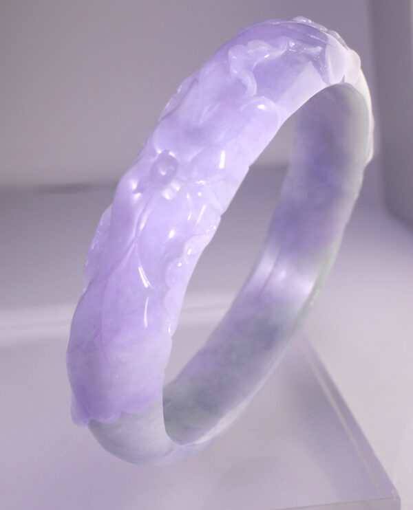 A stunning violet jadeite bracelet featuring intricate relief carvings of traditional auspicious patterns, showcasing the natural gradient and fine-grained texture of the gemstone. The elegant design and lustrous sheen make it a must-have for collectors.