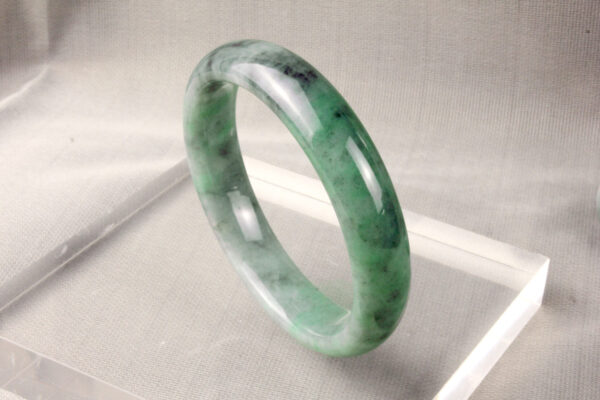 A stunning close-up of the Natural Ice-type Black Chicken Jade Bracelet, showcasing its translucent ice-like clarity, floating green hues, and intricate Black Chicken patterns. The smooth, rounded design elegantly drapes over a wrist, highlighting its refined craftsmanship.