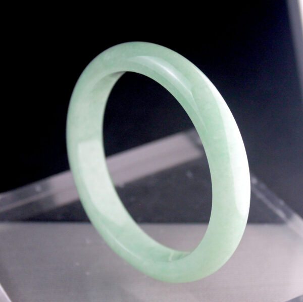 A beautifully polished Natural Douqing Jadeite Bracelet resting on a silk cloth, showcasing its smooth texture and elegant light green hue, symbolizing tranquility and sophistication.