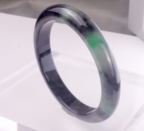A stunning Natural Emerald Ice Jade Bracelet showcasing vibrant green and black-spotted patterns, polished to a smooth, glossy finish. The round-bar design fits comfortably on the wrist, highlighting its natural beauty.