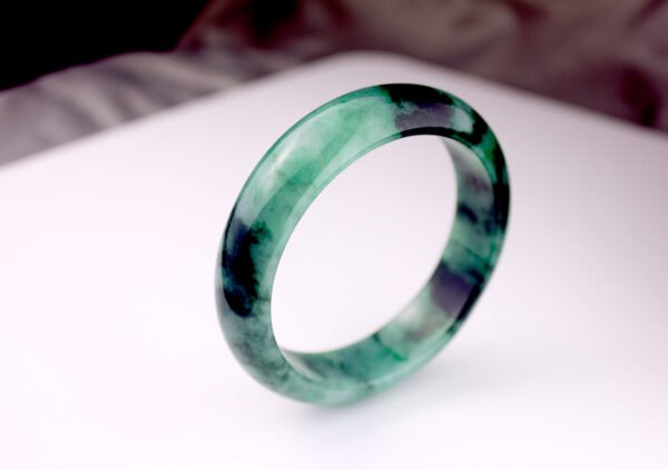 A stunning Natural Ice-Type Flower Jadeite Bracelet showcasing translucent icy luster with vivid green and black floral patterns, elegantly polished for a smooth, comfortable fit.