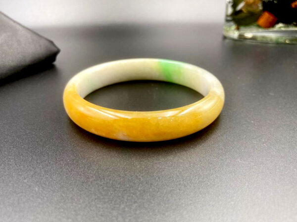 A stunning close-up of the Natural Emerald Yellow-and-Green Bracelet, showcasing its rare yellow-and-green hues, smooth round-bar design, and lustrous glassy finish. The colors transition naturally, resembling honey and jade.