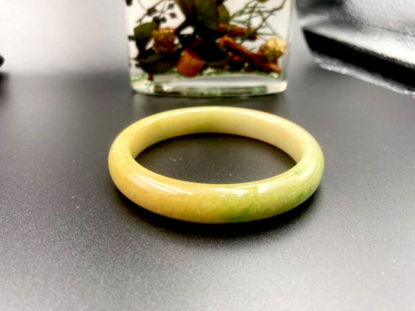 A stunning Natural Yellow-and-Green Jadeite Bracelet with smooth round-bar design, showcasing a seamless blend of tender yellow and lively green hues. The polished edges and fine texture reflect light beautifully, highlighting its traditional craftsmanship.