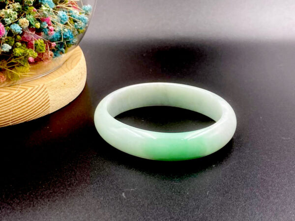 A stunning Natural Yellow-and-Green Jadeite Bracelet with smooth round-bar design, showcasing a seamless blend of tender yellow and lively green hues. The polished edges and fine texture reflect light beautifully, highlighting its traditional craftsmanship.