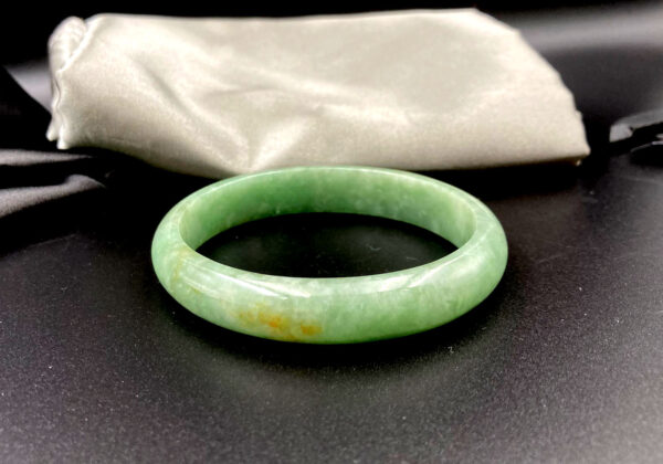 A stunning Natural Dou Green Feicui Concubine Bracelet, showcasing a smooth oval design with a warm dou-green hue and subtle yellow accents, resting elegantly on a velvet display.