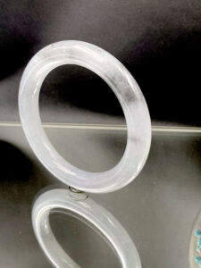 A stunning Natural Ice-type Black Chicken Jadeite Bracelet showcasing its translucent ice-clear base with striking grayish-black ink-like patterns. The smooth round-bar design highlights traditional craftsmanship and modern elegance.