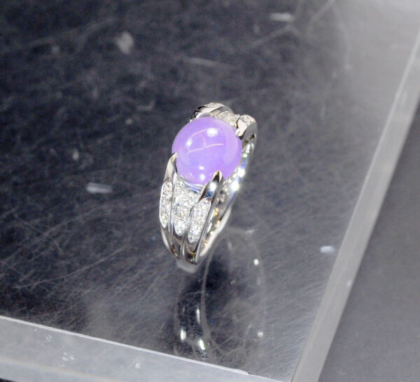 A stunning close-up of the Natural Ice-type Violet Jade Cabochon Ring, showcasing its translucent violet hue, 22K white gold band, and sparkling diamond accents on a velvet background.