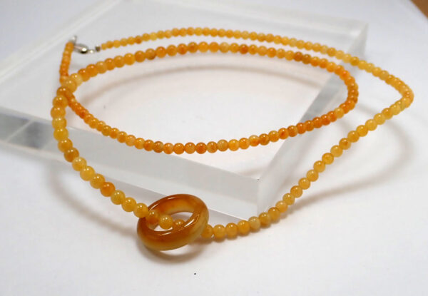 A stunning Natural Ice Yellow Jade Necklace featuring smooth, gradient-hued beads and a polished circular pendant, elegantly draped on a neutral background.