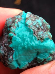 Natural turquoise rough stone with vibrant blue-green hues and black spiderweb veining.