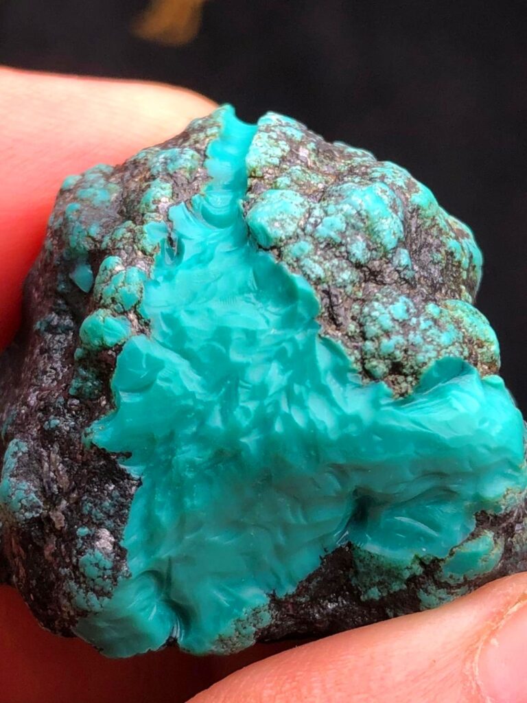 Natural turquoise rough stone with vibrant blue-green hues and black spiderweb veining.