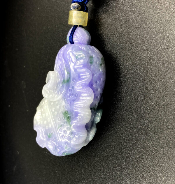 A finely carved violet jadeite pendant in the shape of a Chinese cabbage, showcasing soft purple tones with subtle green spots. The intricate leaf details and smooth polish highlight its natural beauty, elegantly suspended from a blue cord with a yellow bead accent.