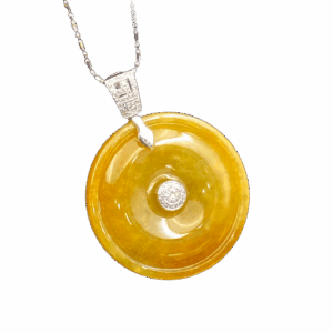 A stunning close-up of the Natural Yellow Jadeite Peace Button Pendant, showcasing its warm amber-like hue, intricate 18K white gold inlay, and sparkling diamond accents. The pendant rests elegantly on a velvet background, highlighting its luxurious craftsmanship.
