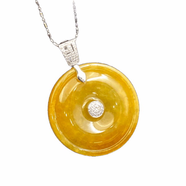 A stunning close-up of the Natural Yellow Jadeite Peace Button Pendant, showcasing its warm amber-like hue, intricate 18K white gold inlay, and sparkling diamond accents. The pendant rests elegantly on a velvet background, highlighting its luxurious craftsmanship.