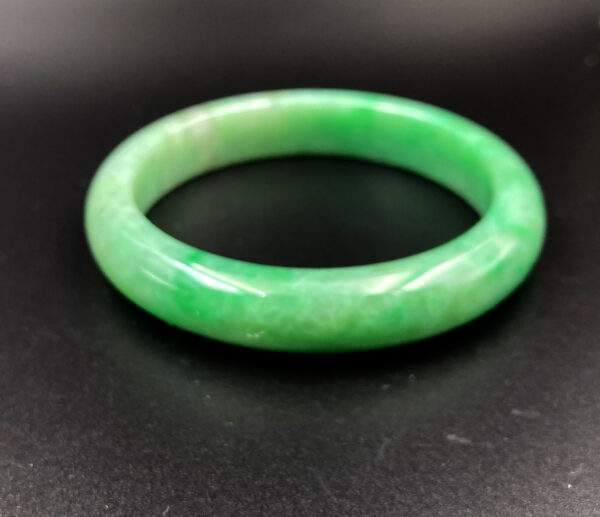 A stunning natural jadeite full green bangle, showcasing a rich, even green hue with icy bean texture. The smooth, polished surface reflects light beautifully, highlighting its classic round design and flawless craftsmanship.