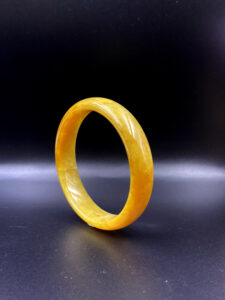 A lustrous honey-yellow jadeite bangle with a flawless, glossy surface, showcasing its natural color gradient and delicate internal structure. The round design fits elegantly on the wrist, reflecting refined craftsmanship.