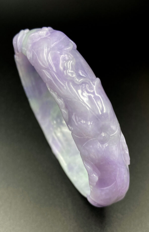 A stunning violet jadeite bracelet featuring intricate relief carvings of traditional auspicious patterns, showcasing the natural gradient and fine-grained texture of the gemstone. The elegant design and lustrous sheen make it a must-have for collectors.
