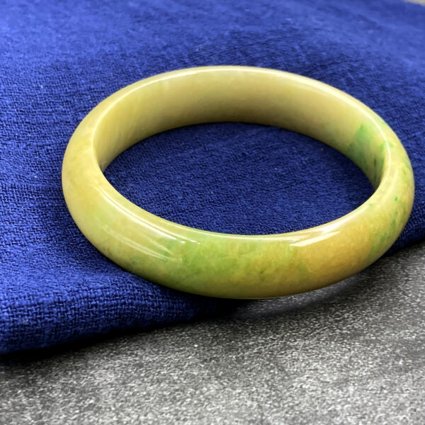 A smooth, polished natural jadeite bangle showcasing a harmonious blend of warm yellow and vibrant green hues. The round-shaped design fits comfortably on the wrist, reflecting light beautifully for an elegant and classic look.
