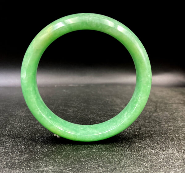 A stunning close-up of a smooth, glossy apple-green jadeite bangle resting on a velvet surface, showcasing its uniform color and flawless craftsmanship.