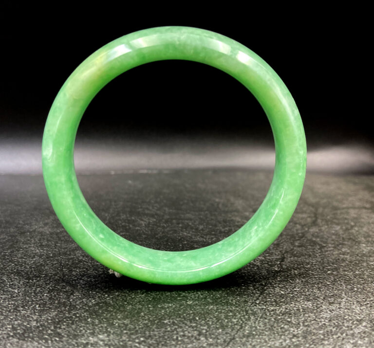 A stunning close-up of a smooth, glossy apple-green jadeite bangle resting on a velvet surface, showcasing its uniform color and flawless craftsmanship.