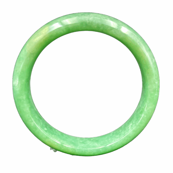 A stunning close-up of a smooth, glossy apple-green jadeite bangle resting on a velvet surface, showcasing its uniform color and flawless craftsmanship.