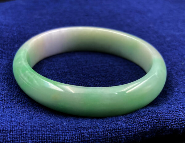 Elegant oval-shaped natural jadeite concubine bracelet with smooth green floating patterns, showcasing subtle gradients on a lustrous translucent surface, resting on a velvet display.