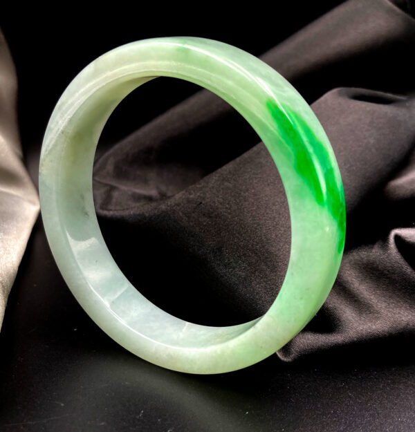 A stunning spicy green jade bangle with intense color and a polished glass-like sheen, resting on a soft fabric background, showcasing its flawless craftsmanship and natural beauty.