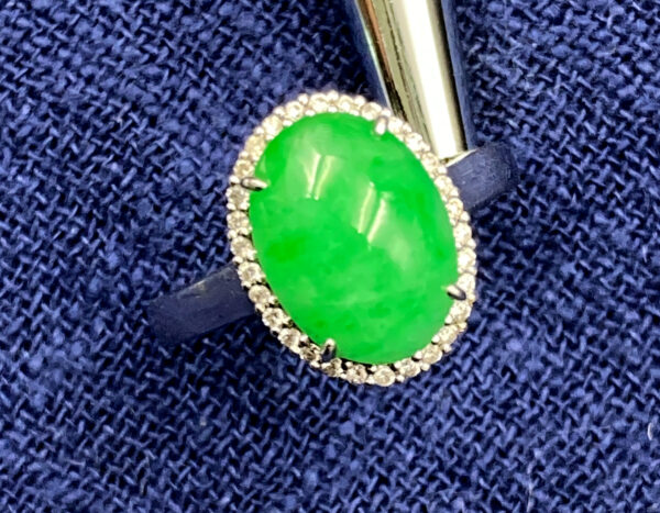 A stunning oval cabochon douqing jadeite ring set in 18K white gold, encircled by dazzling diamonds, showcasing a harmonious fusion of luxury and craftsmanship.