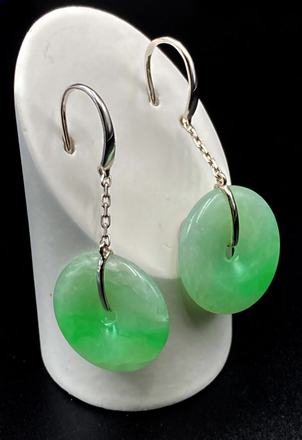 A pair of elegant Ice-Type Jadeite Bean-Green Earrings, showcasing the natural translucency and fine texture of the jadeite. The smooth, polished "Ping An Kou" pendant is securely set in sleek 18K white gold, with a minimalist hook and chain design. The earrings rest gracefully against a neutral background, highlighting their delicate green hue and refined craftsmanship.