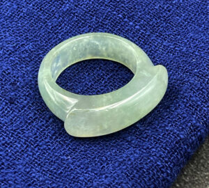 A stunning icy white jadeite saddle ring, showcasing its translucent, smooth texture and elegant saddle-shaped design, resting on a soft fabric background.